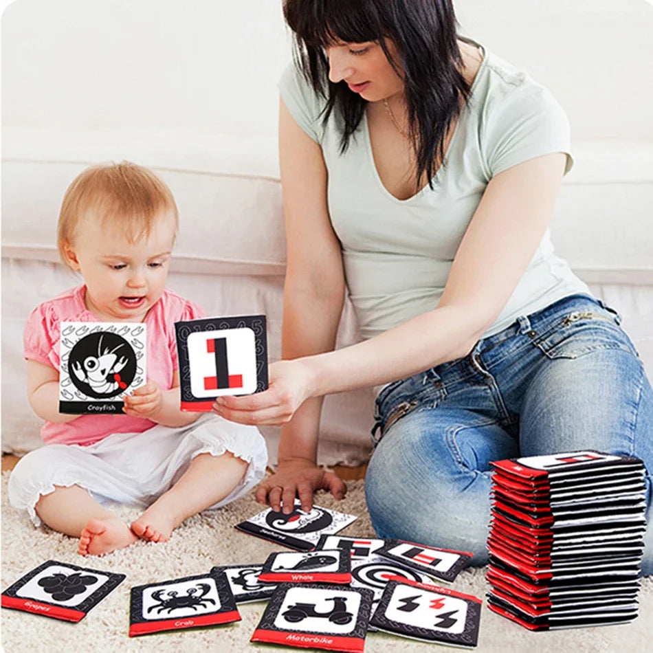 A woman is holding a stack of black and red flash cards featuring letters, numbers, and symbols for baby learning.