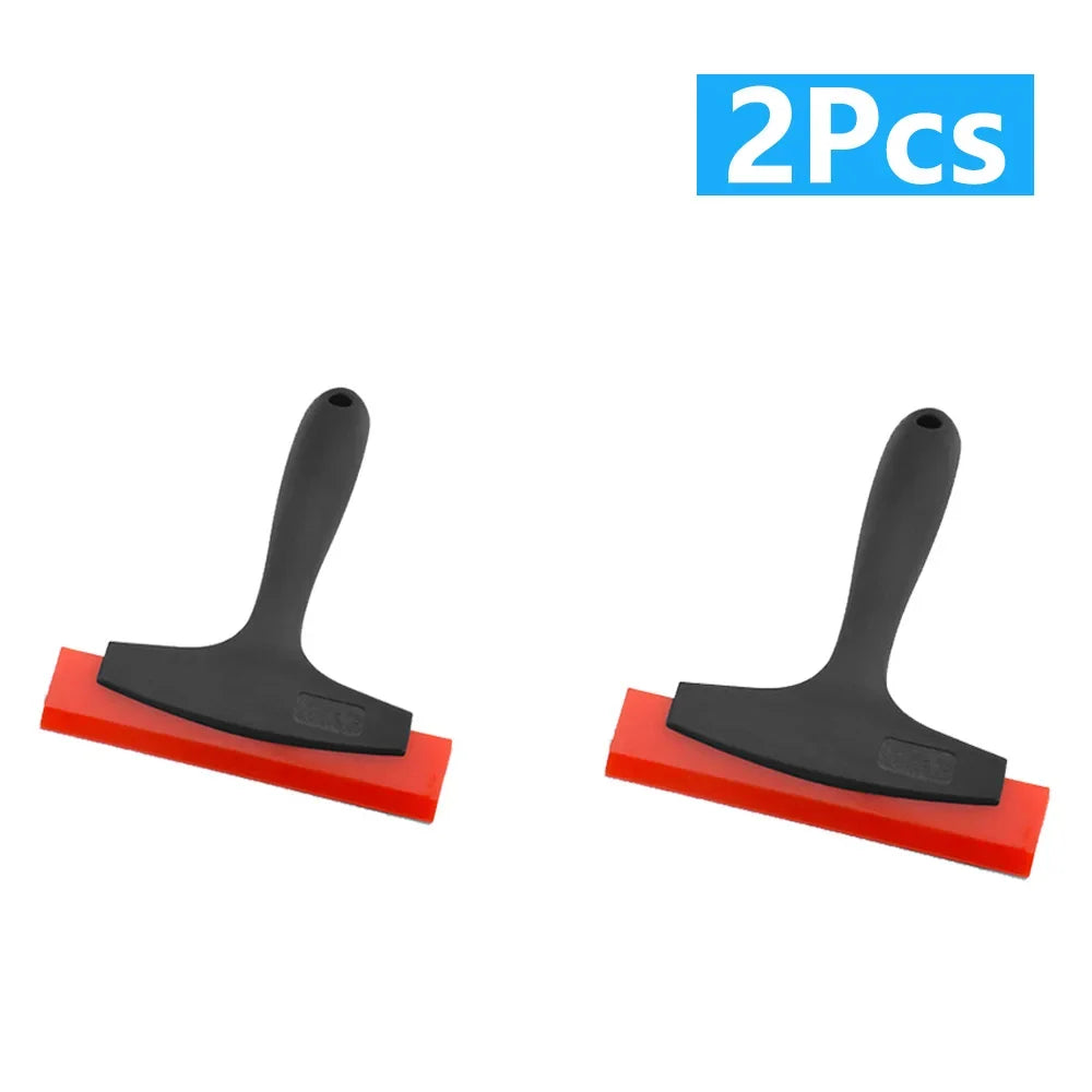 A set of two black tile gap filling and cleaning scrapers with red handles.