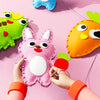 Hands are assembling a pink rabbit plushie and an orange carrot plushie from a sewing kit on a pink background.
