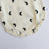 A close-up of a cream-colored baby cotton jumpsuit with black crescent moon patterns.