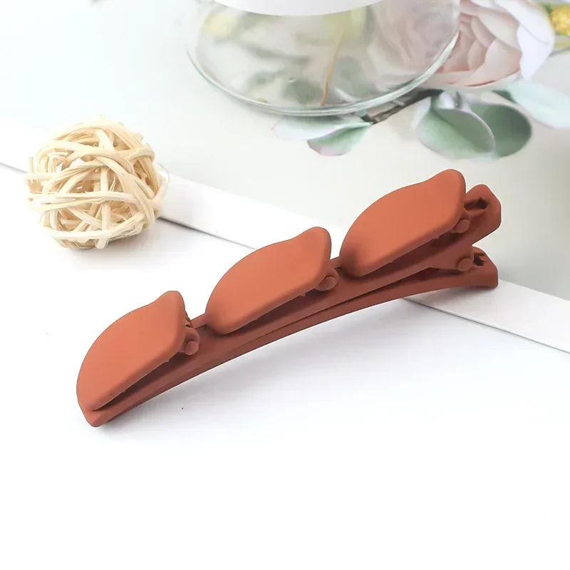 Clip de pelo trenzado de dos capas en color terracota junto a una bola de ligas de pelo claras sobre una superficie blanca.