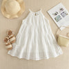 A white cotton dress with eyelet details and a gathered bodice, laid out on a beige fabric next to a straw hat and some shoes