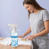 A woman is applying a bottle of clothing stain remover spray onto a white cloth.