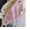 A display of various knitted cardigan sweaters in pastel colors, including cream, yellow, and pink, hanging on a wooden rack.