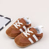 A pair of brown suede baby first walker shoes with white stripes and white soles resting on a light background.
