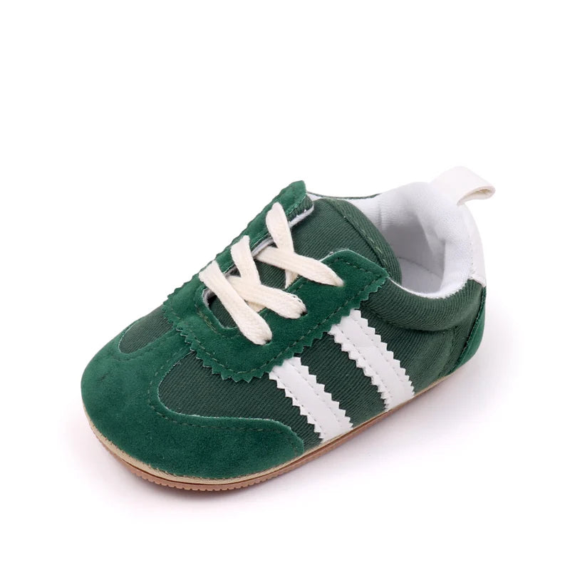 A pair of green baby first walker shoes with white laces and white stripes on the side