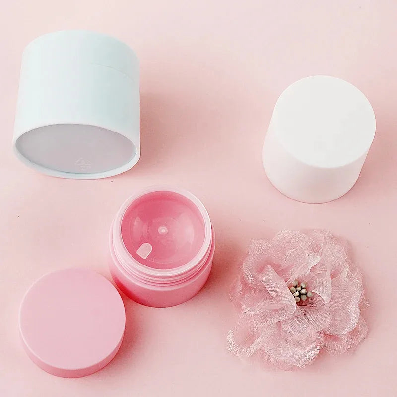 Pink refillable travel face cream jars with white lids and a pink tissue