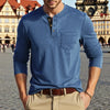 A man wearing a blue long-sleeve casual shirt with a chest pocket and tan pants standing outdoors.