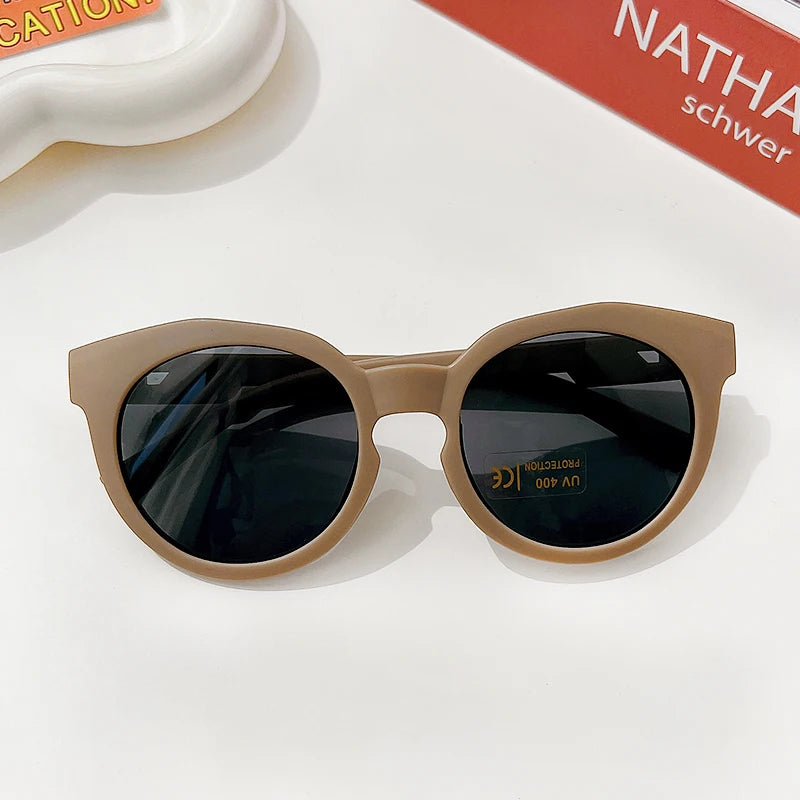 A pair of light beige sunglasses with dark lenses resting on a white surface.