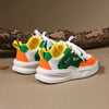 A pair of yellow and green casual sneakers with white laces and thick white soles resting on a brown log.