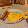 A plate with fried duck-shaped rice molds, a sliced cucumber, and yellow plastic utensils.
