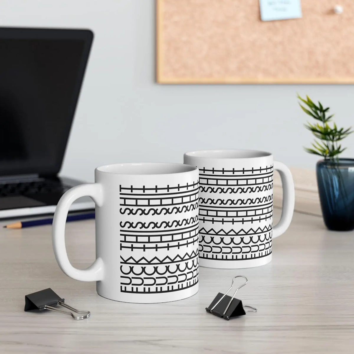 To hvide keramiske kaffekrus med sorte geometriske mønstre på en lys overflade.