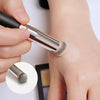 A hand is using a precision makeup brush to apply product on skin.