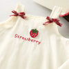 A cream-colored kids summer pinafore dress featuring a strawberry and bunny print detail.