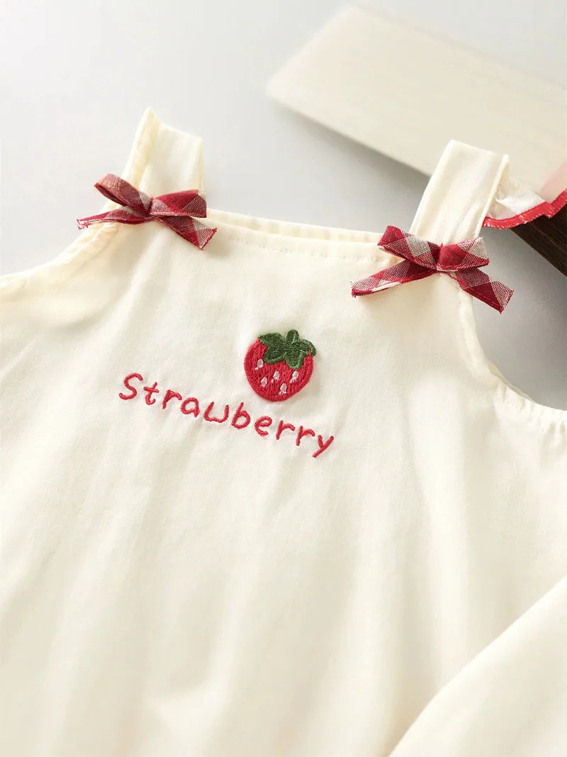 A cream-colored kids summer pinafore dress featuring a strawberry and bunny print detail.