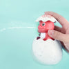 A hand is holding a white bath toy shaped like a duck with a spray feature above a larger egg-shaped body, near light blue wa