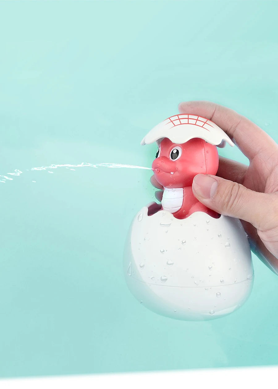 A hand is holding a white bath toy shaped like a duck with a spray feature above a larger egg-shaped body, near light blue wa