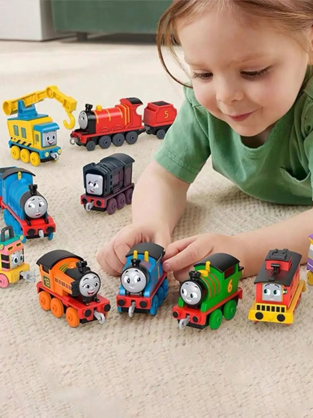 A young child is interacting with various Thomas & Friends diecast train engine toys on a light-colored carpet.