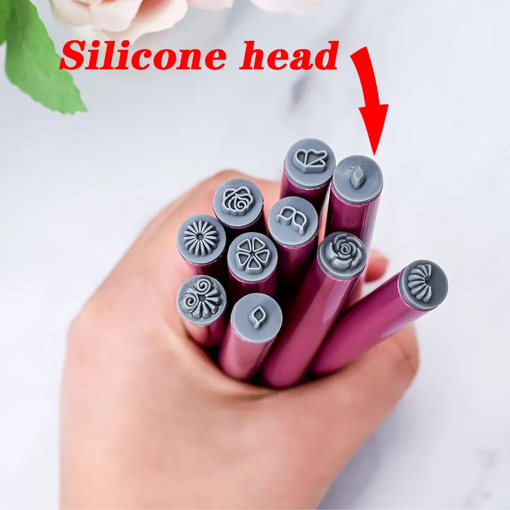 En hånd holder et sett med silikonhoder for neglekunststempling, med ulike blomster- og sommerfugldesign.