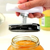 A hand holds a white and silver adjustable jar and bottle opener tool above an orange liquid in a glass jar.