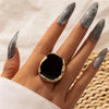 A hand wearing a geometric adjustable acrylic ring with an oval black design on a finger.