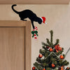 Schwarze Katzen-Silhouette mit rotem Weihnachtsmannhut und grüner Schleife an einer hellen Wand über Holz