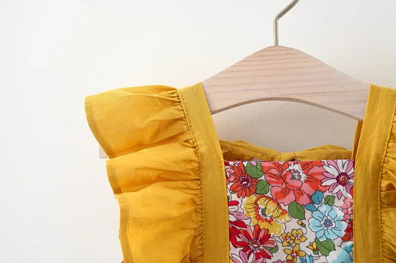 A yellow dress with a floral print bodice and matching yellow trim is displayed on a wooden hanger.