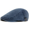 Gorra de estilo newsboy en mezclilla azul oscuro deslavada, con visera doblada y detalle de cuero.