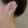 A close-up of a woman's ear adorned with a sparkling butterfly zircon ear cuff and a dangling gold tassel earring.
