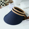 A navy woven straw sun hat with a beige and black striped brim resting on a white surface.