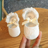 A pair of white lace baby first walker shoes with yellow ribbon on a wooden table.