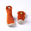 A pair of orange baby first walker socks with a yellow fish design and soft soles.