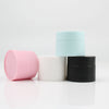 Three cosmetic jars in pink, light blue, and black with white lids arranged on a white surface.