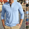 A man wearing a light blue long-sleeve casual shirt with a chest pocket, standing outdoors.