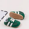 A pair of green and white baby first walker shoes with a brown anti-slip sole are shown on a light background.