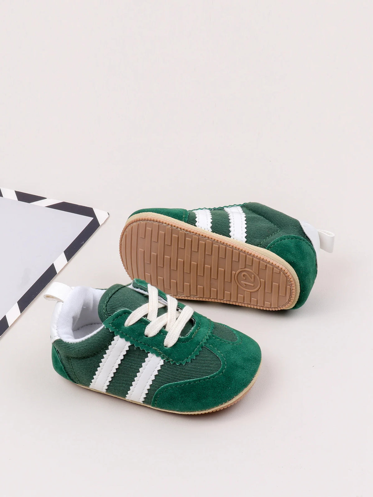 A pair of green and white baby first walker shoes with a brown anti-slip sole are shown on a light background.