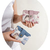 A hand holds a pink floral print women's wallet with a zipper and card slots against a light background.