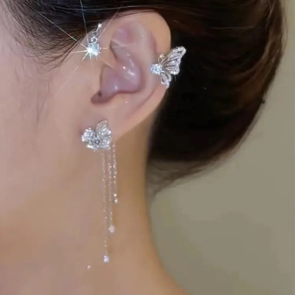 A close-up of a woman's ear adorned with a sparkling butterfly zircon ear cuff and gold tassel earrings.