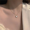A close-up of a silver heart pendant necklace with small crystals and a delicate chain worn on a woman's neck.