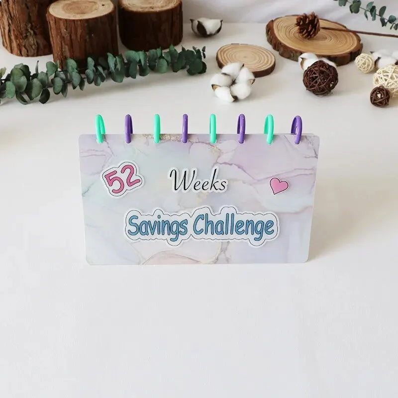 A purple and green binder with 52 weeks marked for a savings challenge, displayed on a white surface.