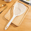 A white long-handled kitchen strainer spoon with a perforated surface rests on a wooden cutting board.
