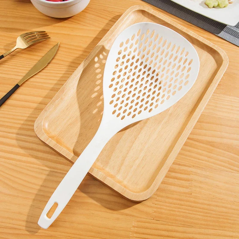A white long-handled kitchen strainer spoon with a perforated surface rests on a wooden cutting board.