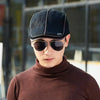 A man wearing a dark knit wool newsboy cap and sunglasses, looking directly at the camera.