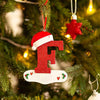 Rød og hvit nisselueformet ornament med bokstaven F henger på en grønn juletregren.