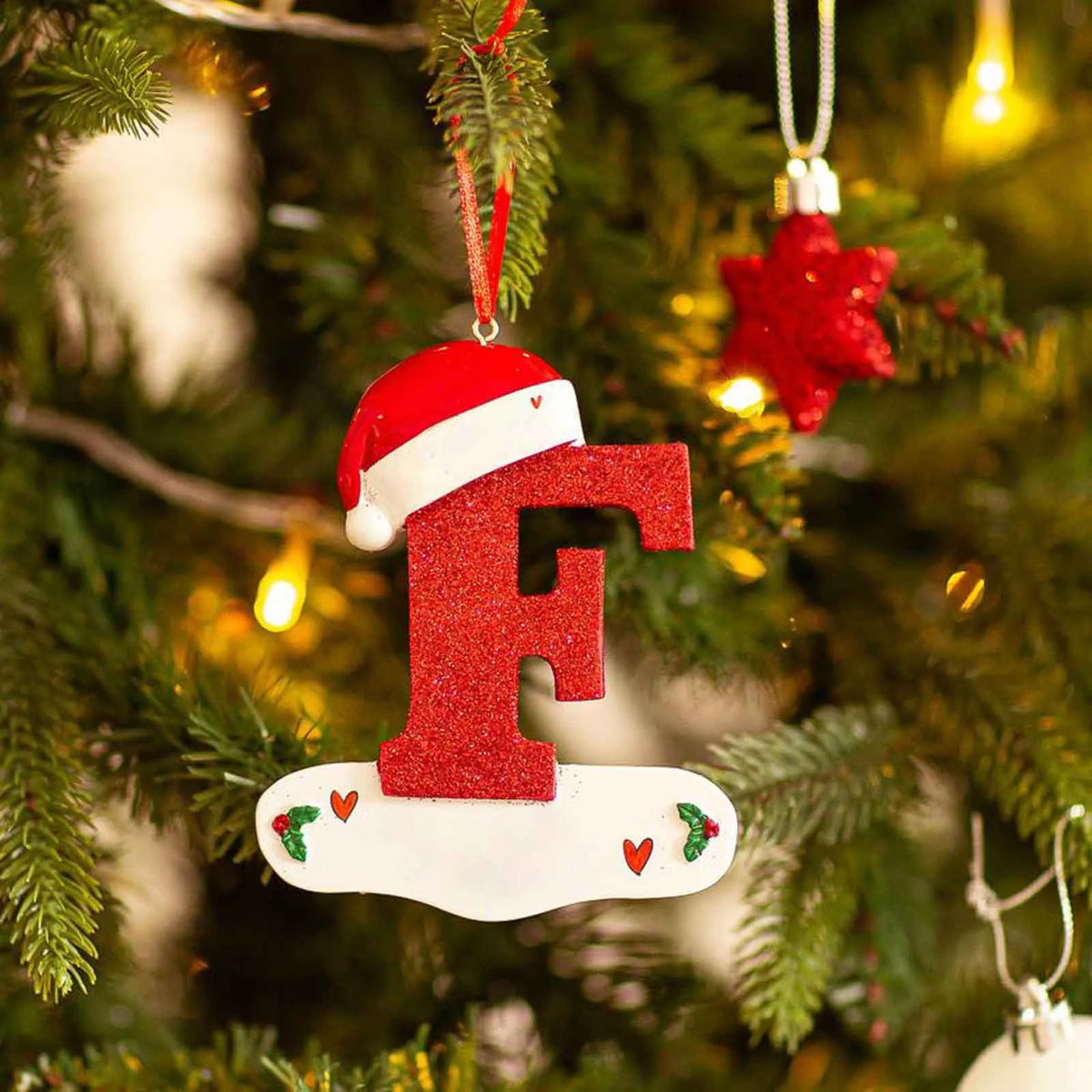 Rød og hvit nisselueformet ornament med bokstaven F henger på en grønn juletregren.