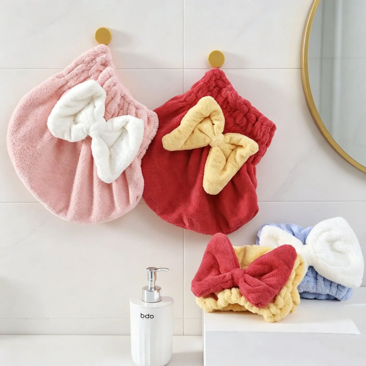 Juego de gorros de microfibra rosas y rojos con lazos blancos y amarillos colgados en una pared de azulejos blancos.
