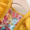 A yellow dress with a floral print bodice and ruffled sleeves is displayed on a wooden hanger.
