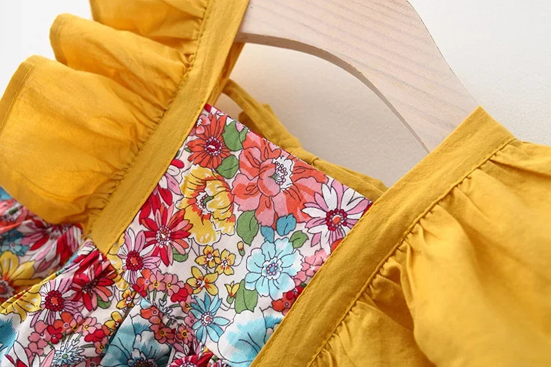 A yellow dress with a floral print bodice and ruffled sleeves is displayed on a wooden hanger.