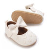 A pair of white soft non-slip baby first walker shoes with a bow detail and a tan sole.
