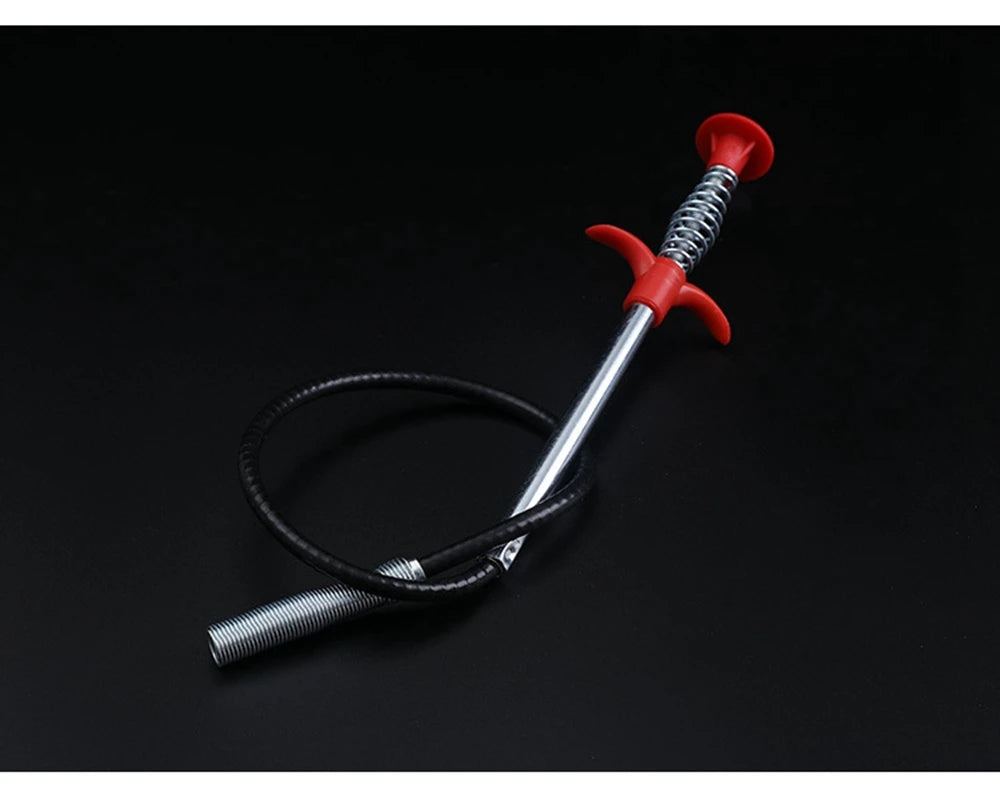 A red flexible drain snake with a metal shaft and black hose coiled on a dark surface.